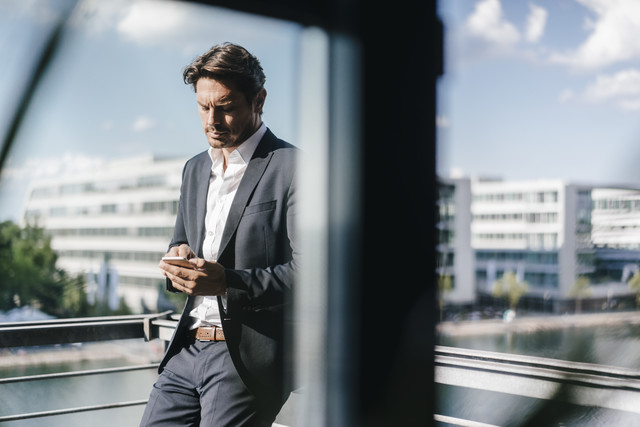 Stockfoto, lizenzfrei, Geschäftsmann steht auf dem Balkon und hält ein Smartphone