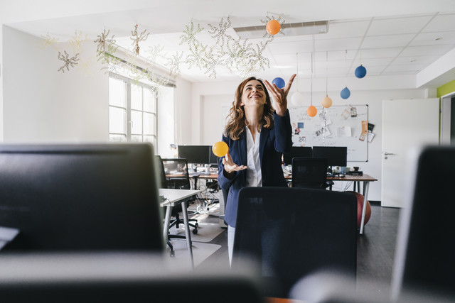 Stockfoto, lizenzfrei, Glückliche Geschäftsfrau jongliert im Büro mit Bällen