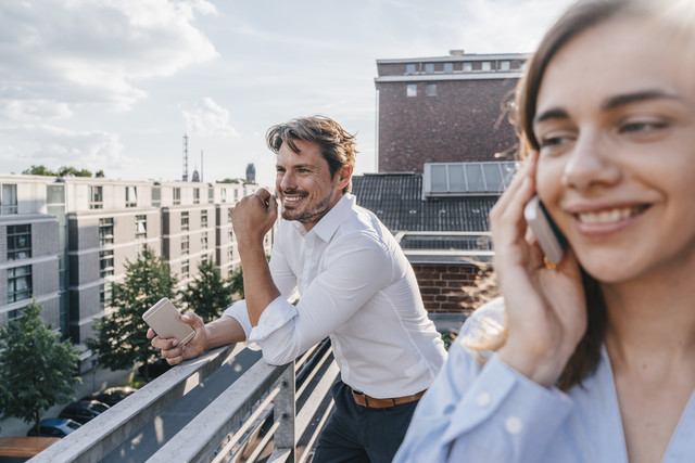 Lizenzfreies Stockfoto,Geschäftsleute, die auf dem Balkon stehen und ein Smartphone benutzen