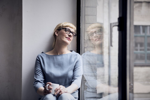Stockfoto, lizenzfrei, Porträt einer lächelnden Frau mit Kaffeetasse beim Blick durchs Fenster
