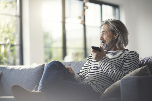 Stockfoto, lizenzfrei, Älterer Mann sitzt auf dem Sofa und benutzt ein Smartphone