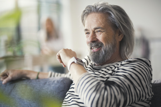 Stockfoto, lizenzfrei, Älterer Mann sitzt auf der Couch und redet mit der Smartwatch