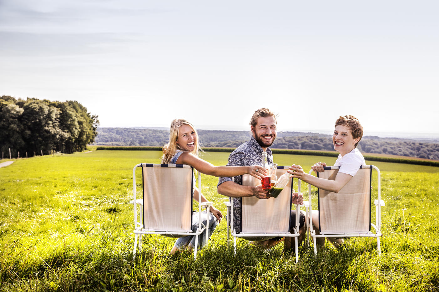 Happy friends sitting on camping chairs in rural landscape clinking bottles
Royalty free image