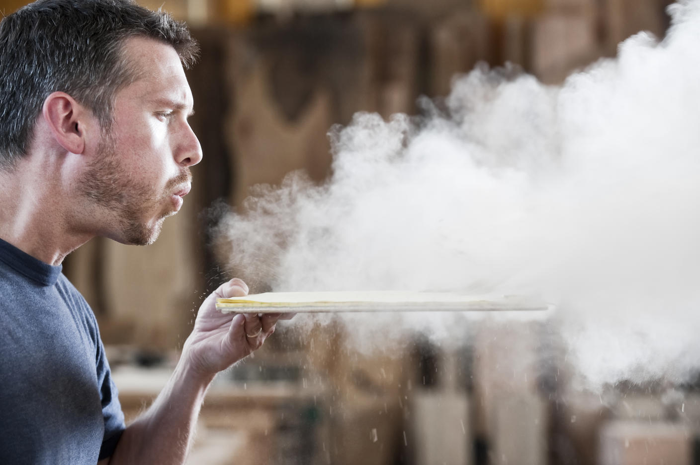 Caucasian man factory worker blowing sanding dust off a wooden piece in a woodworking factory.
Royalty free image