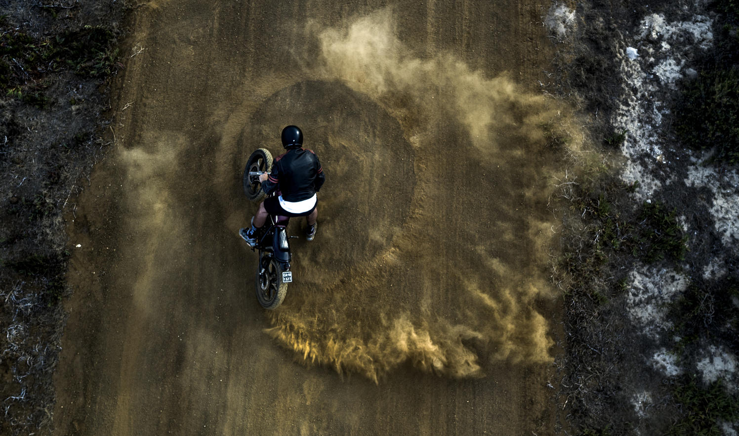 High angle view of man driving cafe racer motorcycle in circles on a dusty dirt road.
Royalty free image