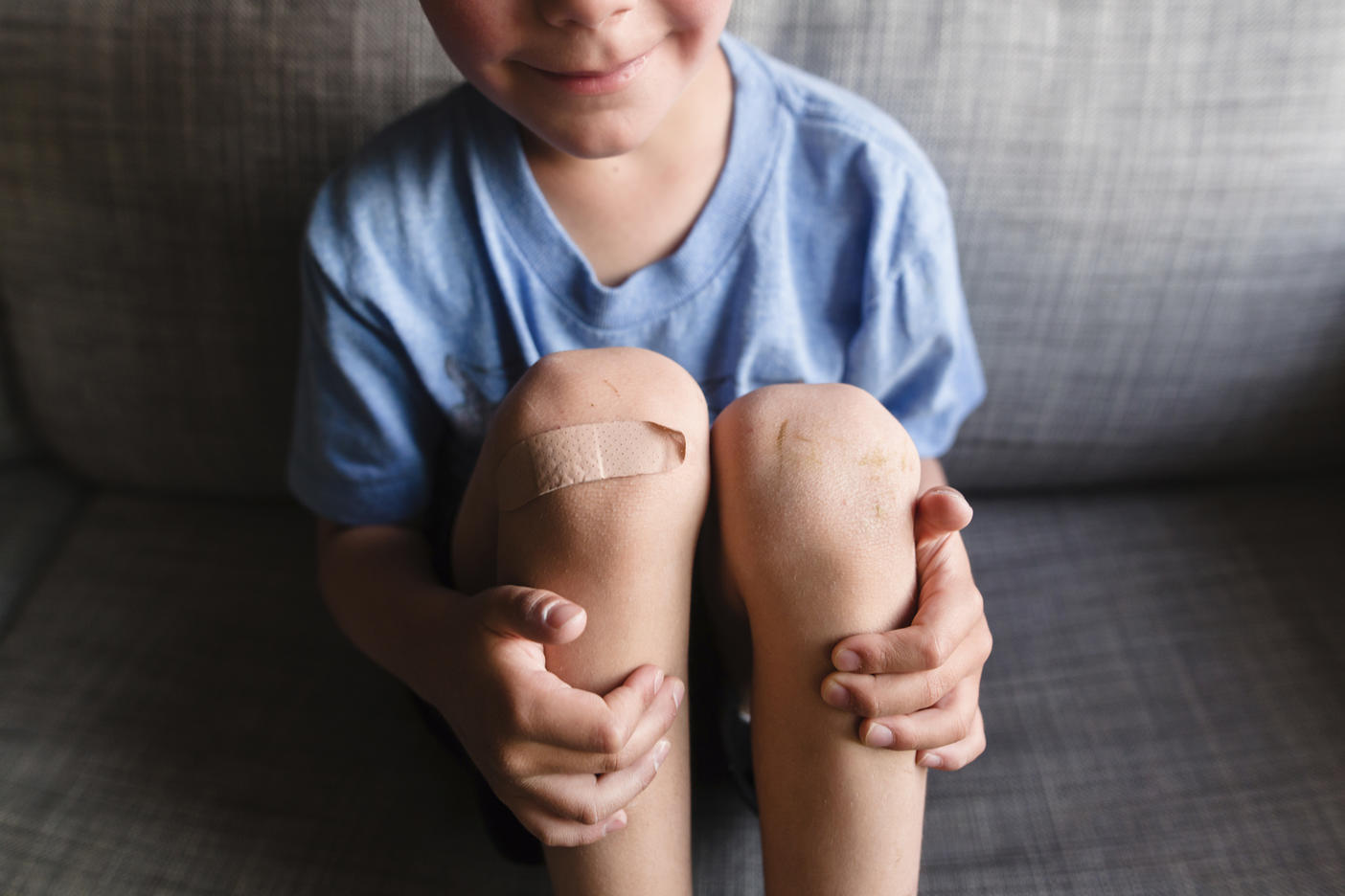 High angle view of boy wearing blue T-shirt sitting on a sofa, a plaster on his right knee.
Royalty free image
