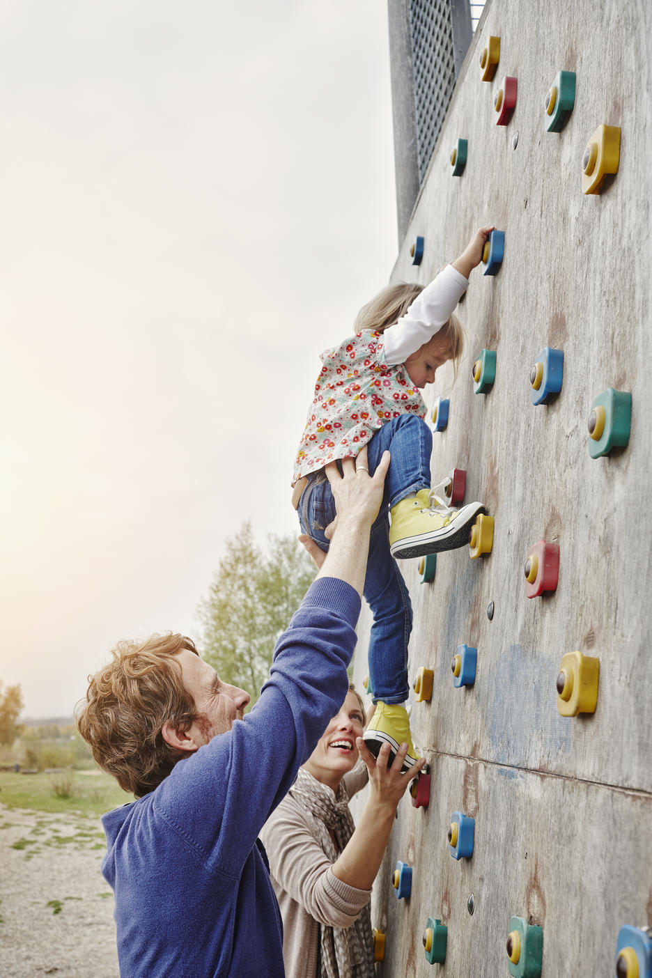 Girl climbing on a wall supported by parentsRoyalty free image