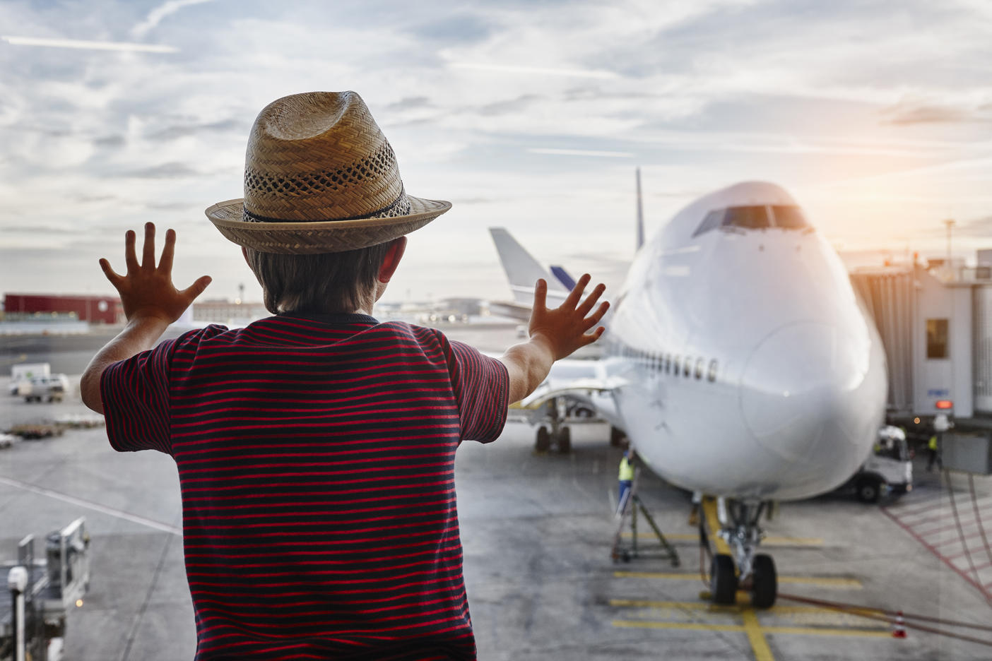 Boy wearing straw hat looking through window to airplane on the apronRoyalty free image