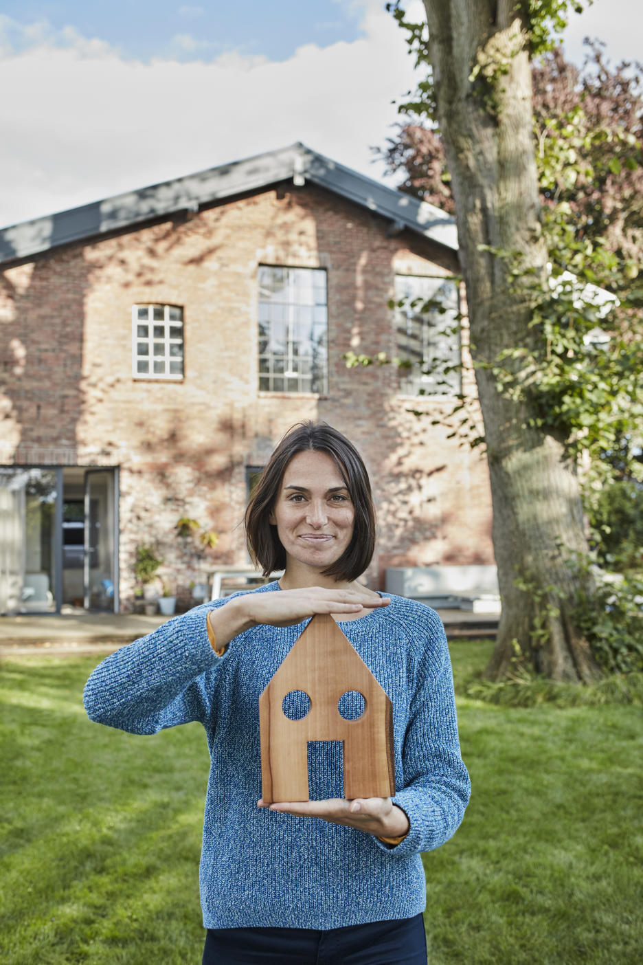 Portrait of smiling woman in garden of her home holding house modelRoyalty free image