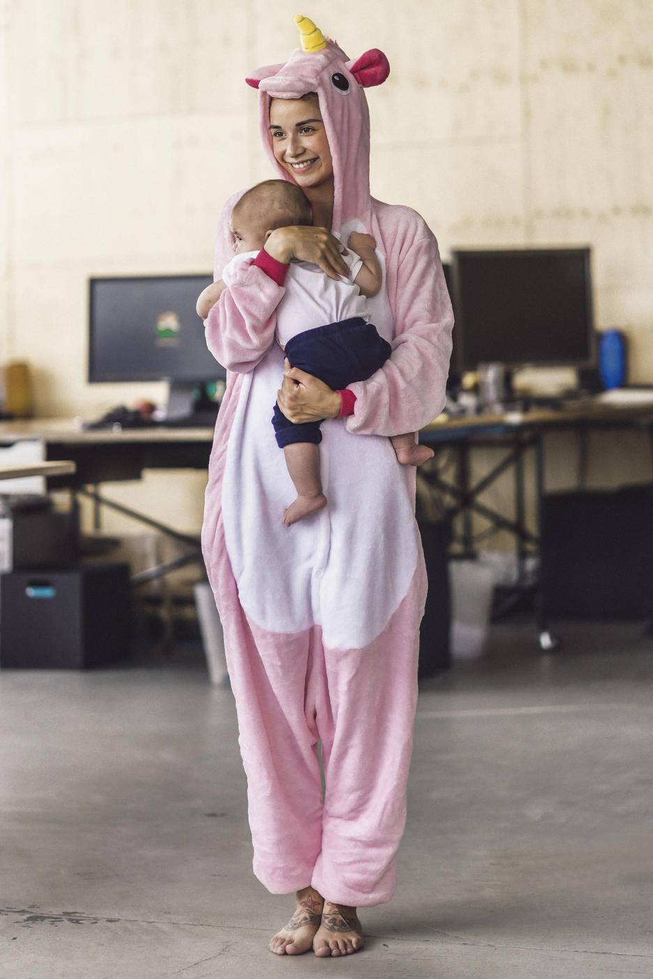 Young mother wearing unicorn onesie, standing in office, holding her son in her arms
Royalty free image