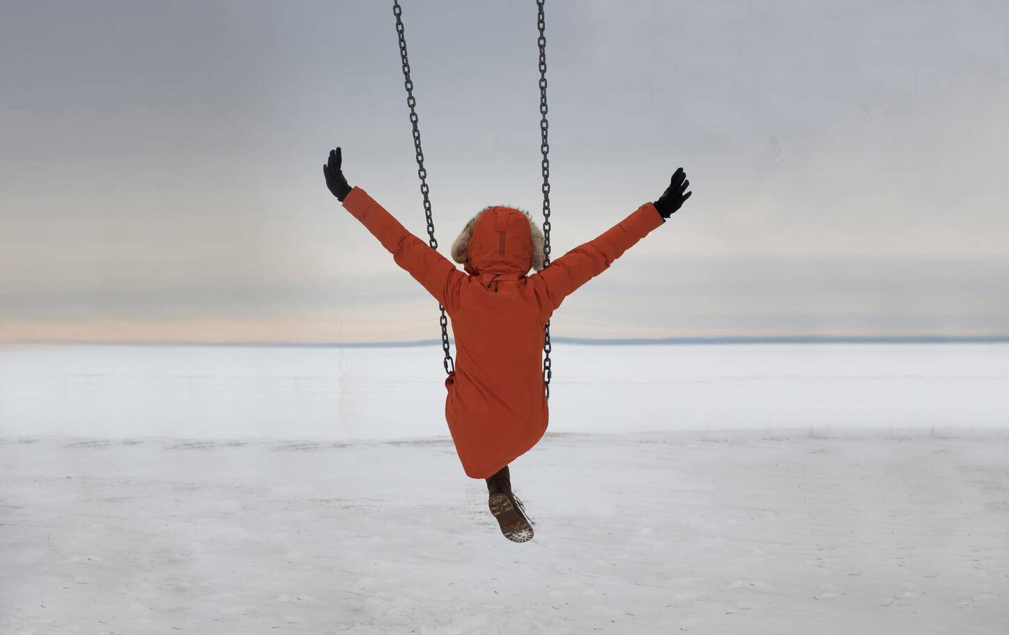 Rear view of woman with arms outstretched swinging over snow covered landscape against cloudy sky
Royalty free image