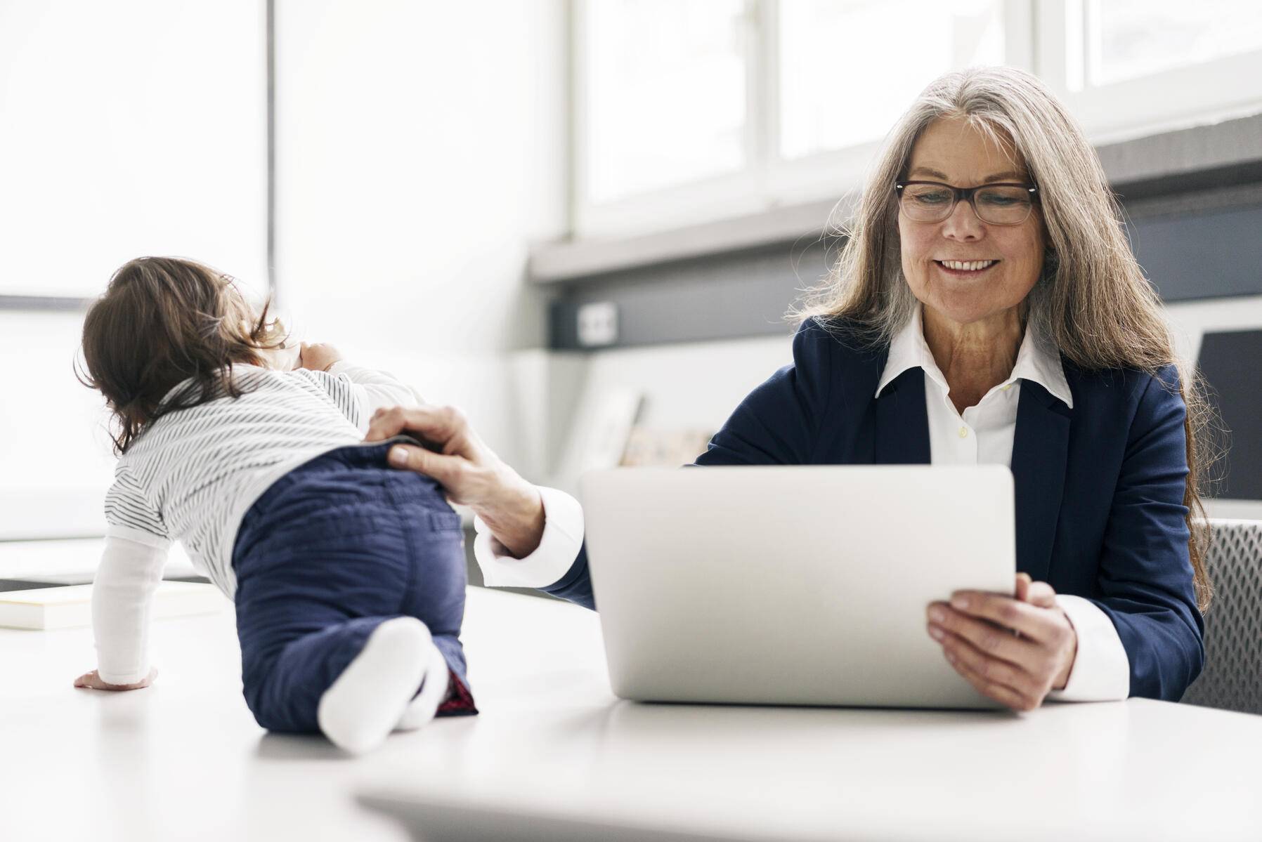 Senior businessswoman sitting at conference table with laptop and baby girl
Royalty free image