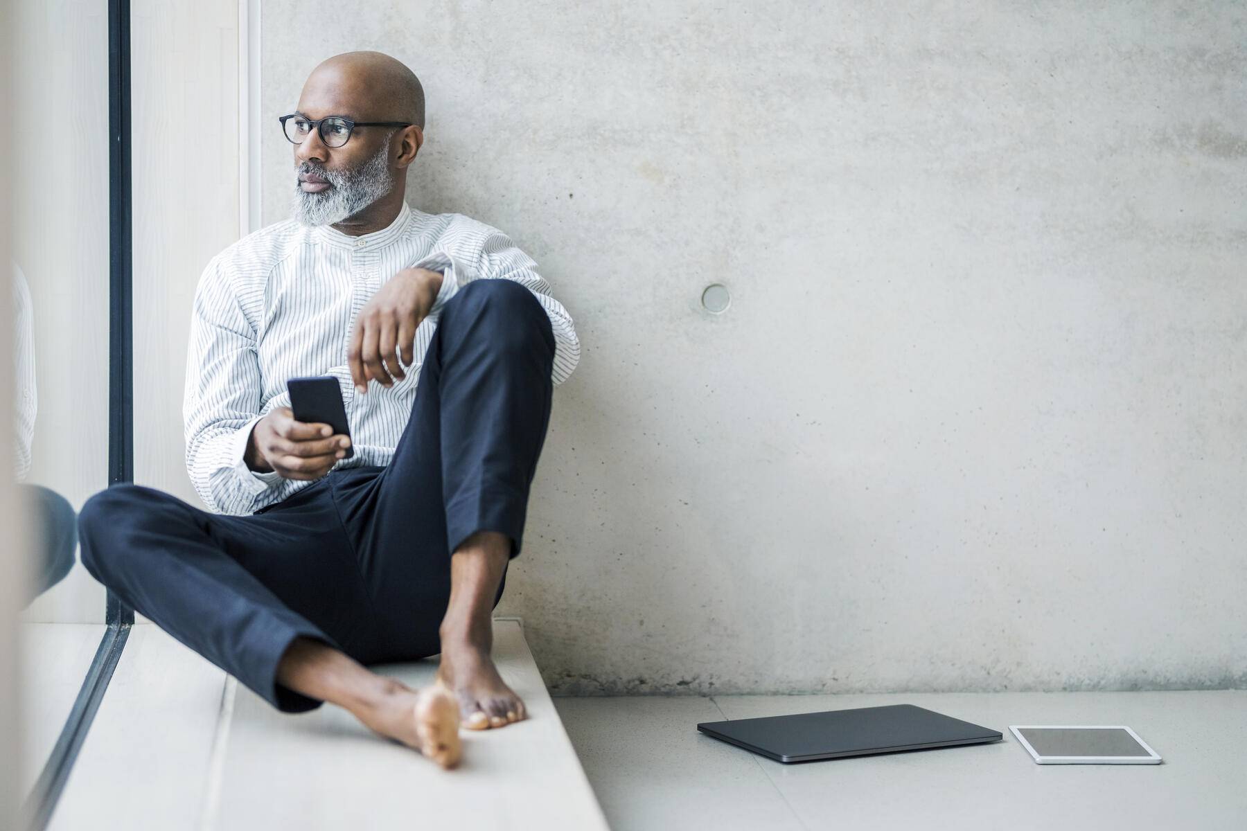 Barefoot mature businessman with smartphone sitting on window sill looking at distance
Royalty free image