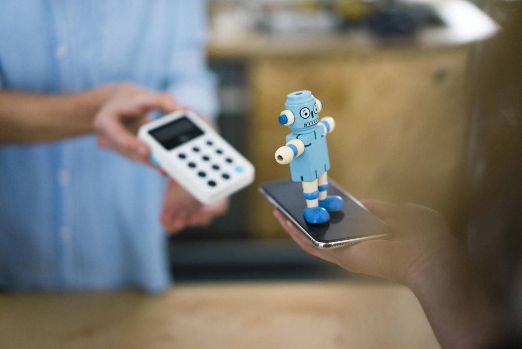 Customer paying contactless in a coffee shop, balancing toy robot on smartphone - JOSF03354