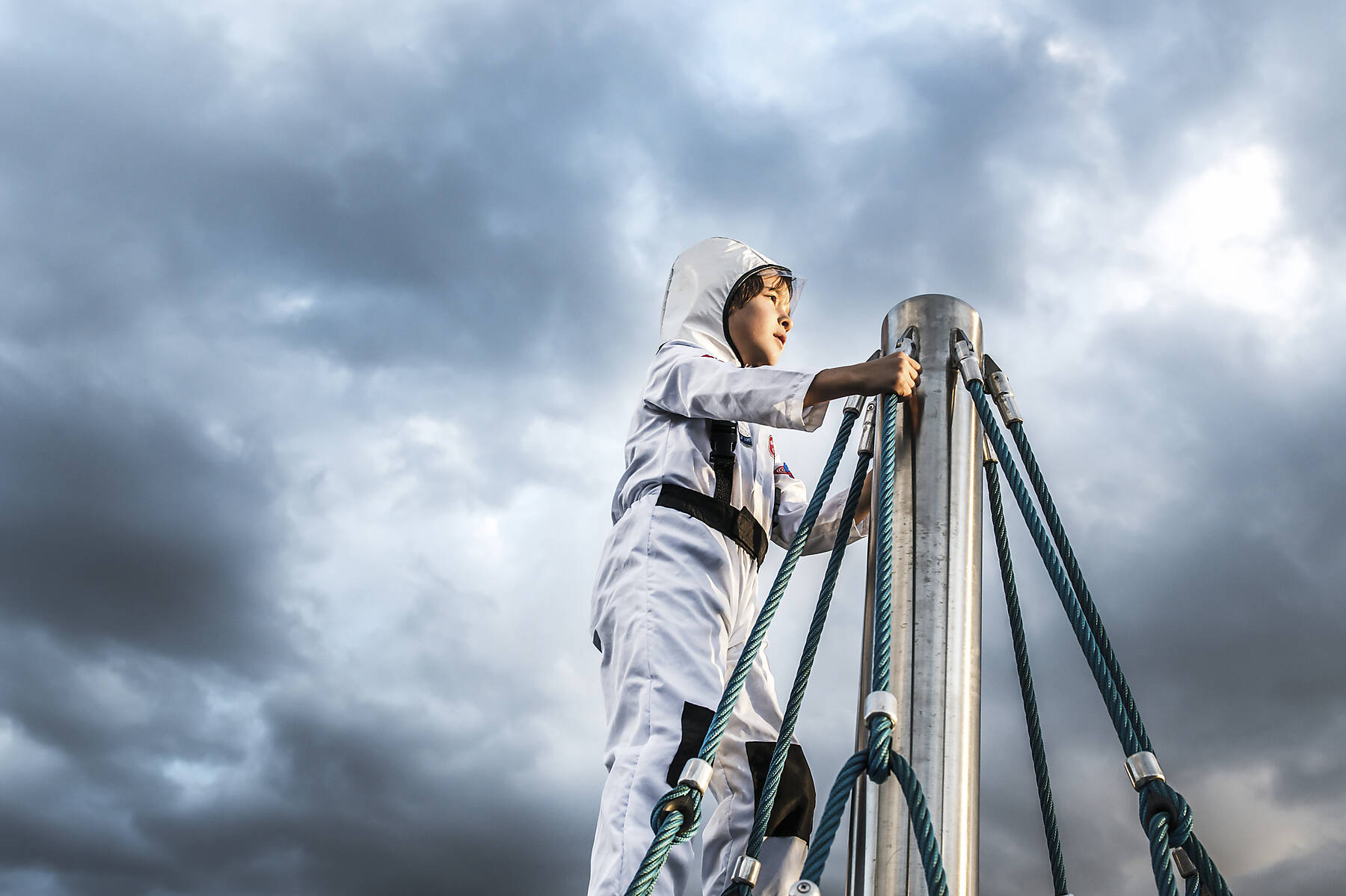 stock image, royalty-free, Boy in astronaut costume gazing from top of climbing frame against dramatic sky