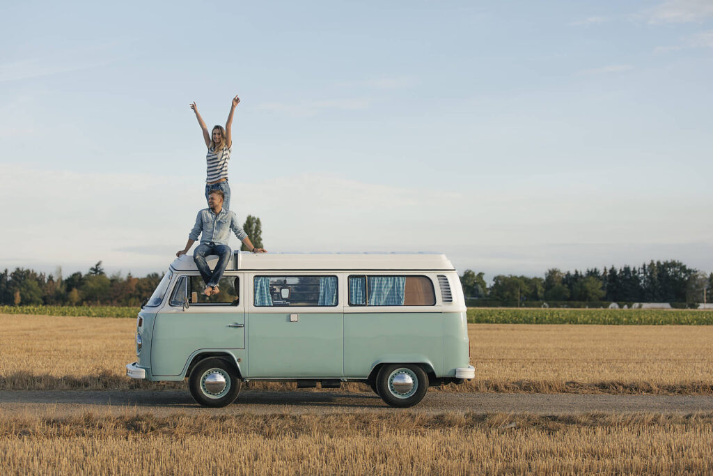 Happy couple on roof of a camper van in rural landscape, stock image, royalty-free