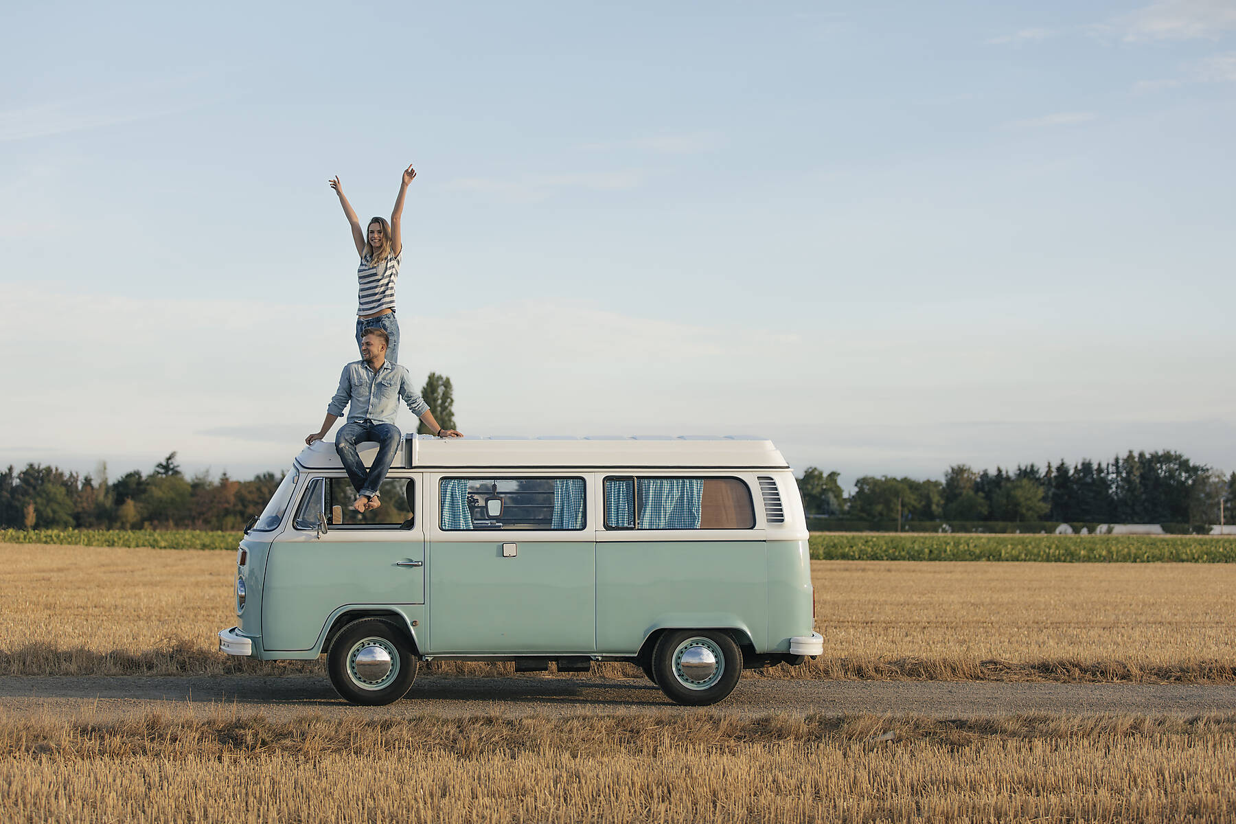Stockfoto, lizenzfrei, Glückliches Paar auf dem Dach eines Wohnmobils in ländlicher Landschaft