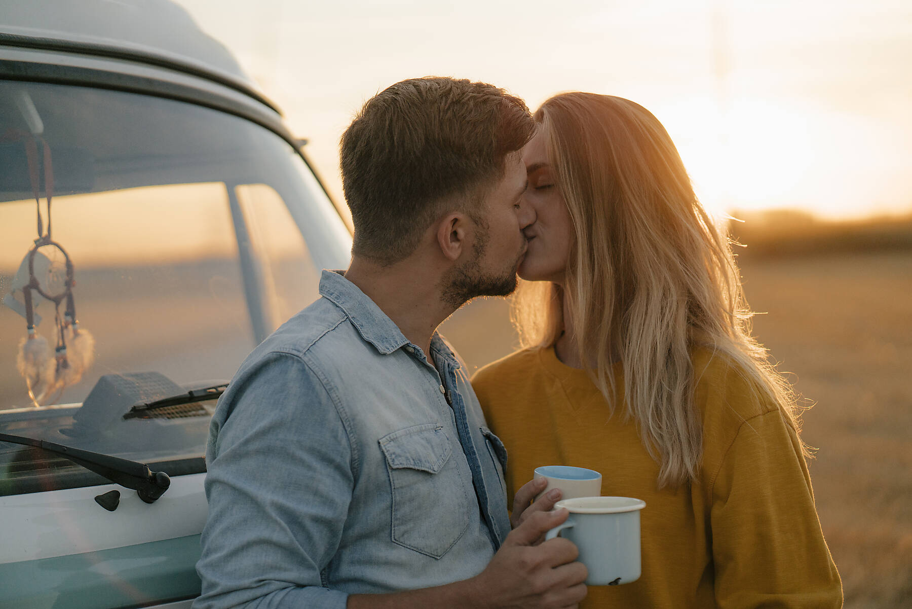 Junges Paar küsst sich am Wohnmobil in ländlicher Landschaft, stockfoto, lizenzfrei,
