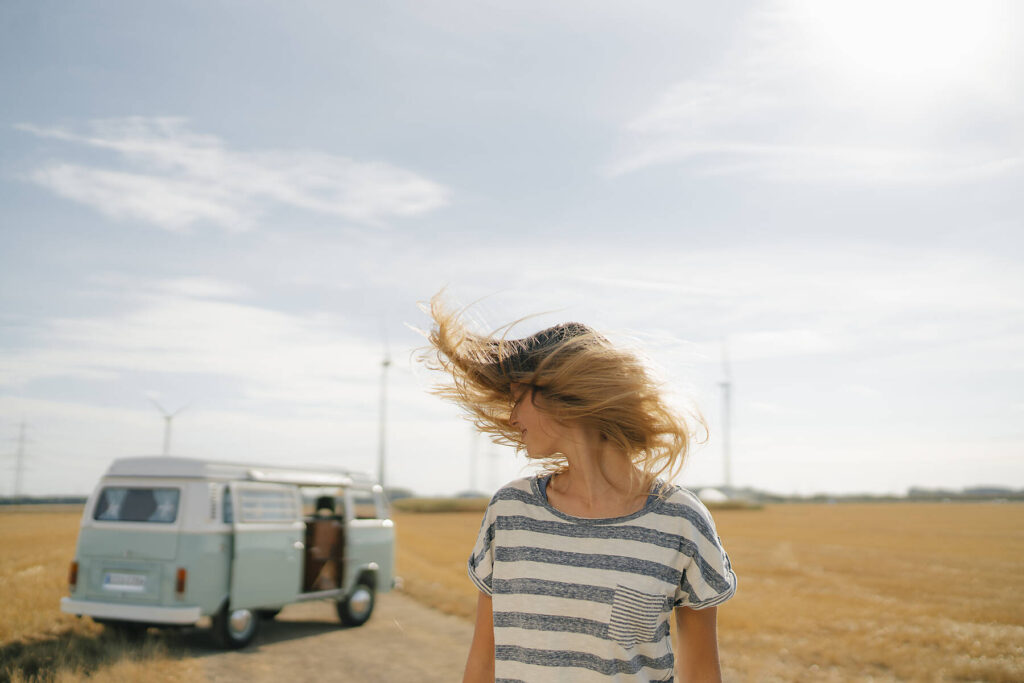 stock image, royalty-free, Blong young woman at camper van in rural landscape shaking her hair