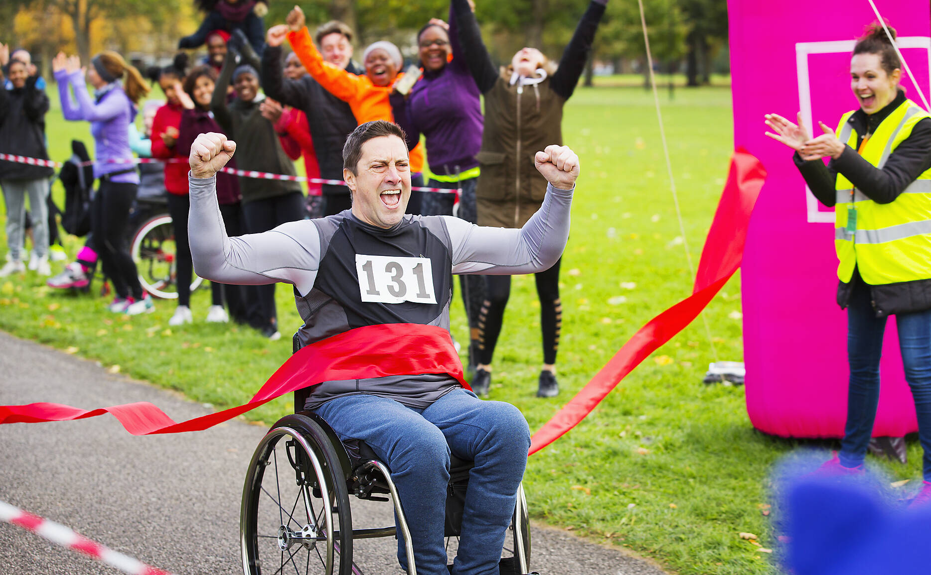stockfoto, lizenzfrei, Begeisterter Mann im Rollstuhl überquert die Ziellinie bei einem Wohltätigkeitsrennen im Park