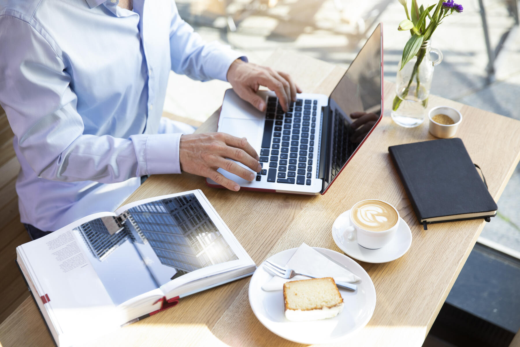 stockfoto, lizenzfrei, Nahaufnahme eines Mannes mit Laptop in einem Cafe mit einem Buch auf dem Tisch