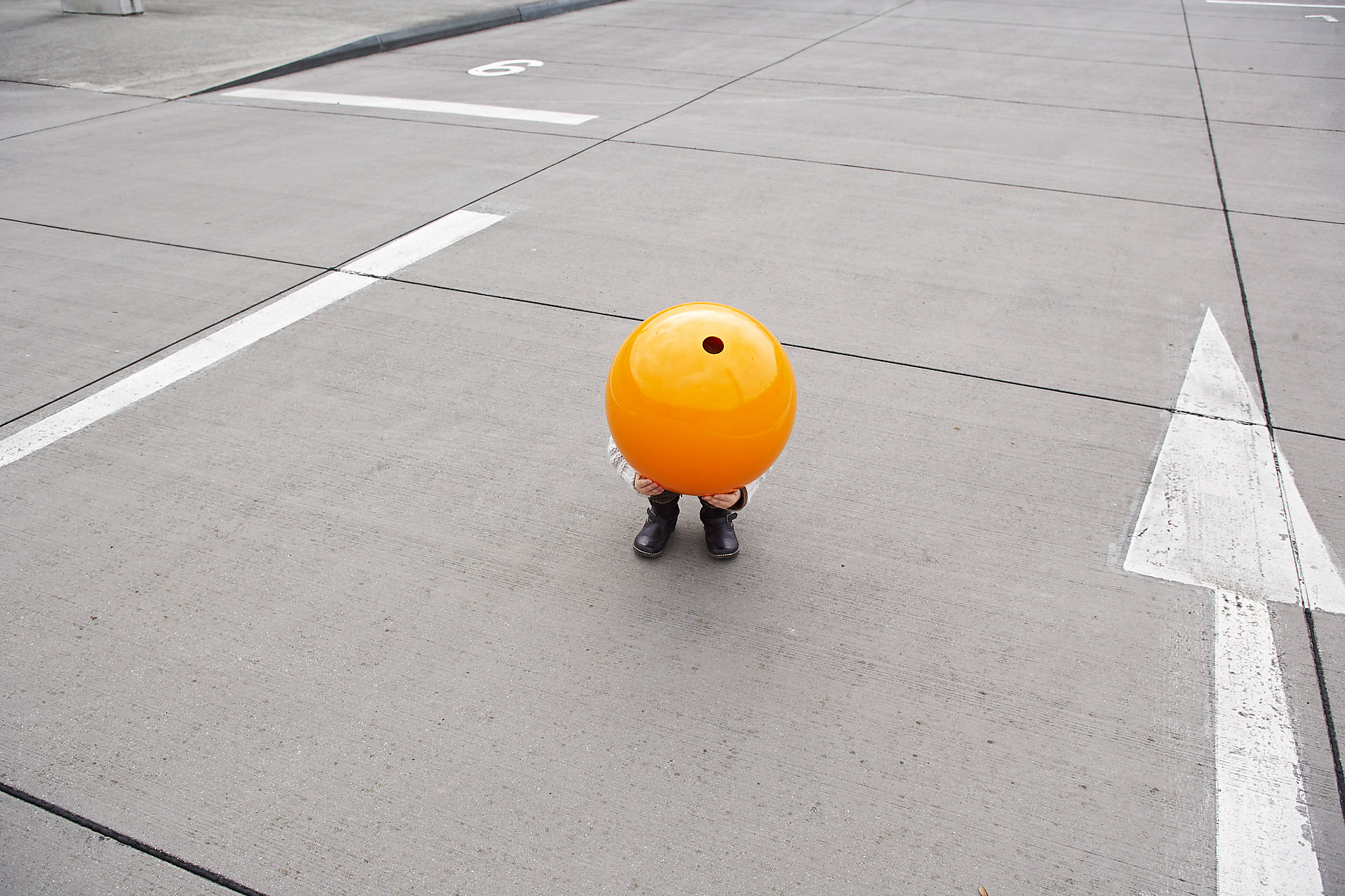 Little girl crouching on the street hiding under orange ball, stock photo, royalty free, safety, protection