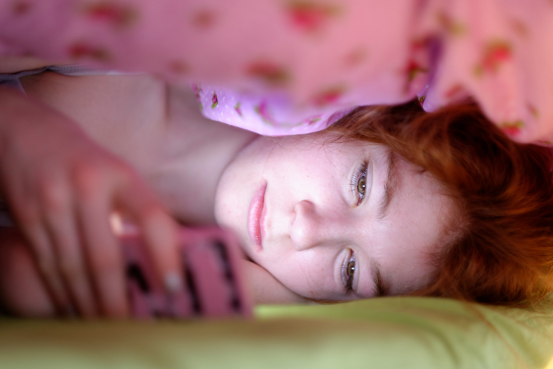 Portrait of girl lying under blanket in bed looking at her smartphone, stock photo, royalty free, safety, security