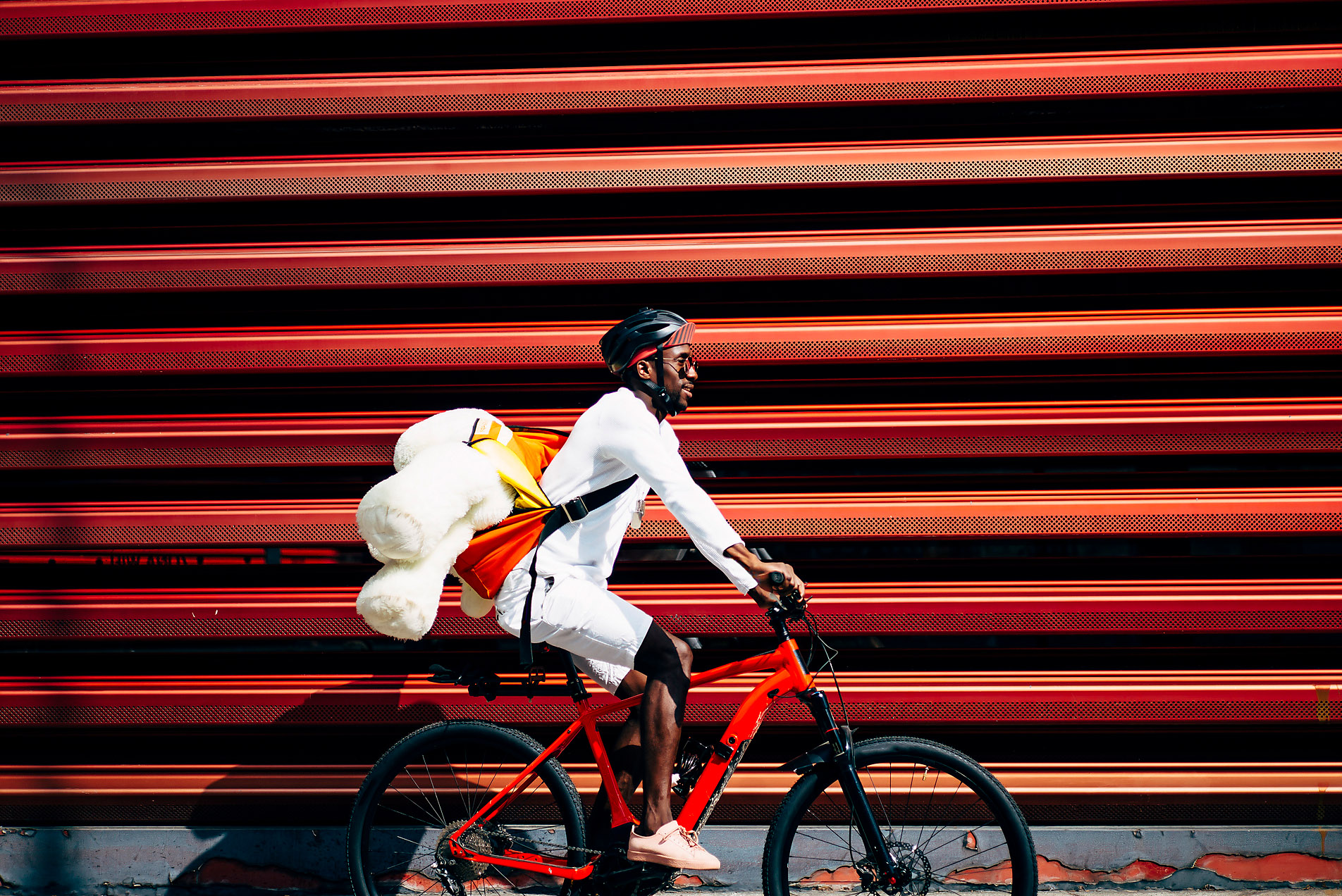 Bicycle courier delivering a teddy bear passing a red wall, Mobility, protection, security, Westend61, stock photo, royalty free