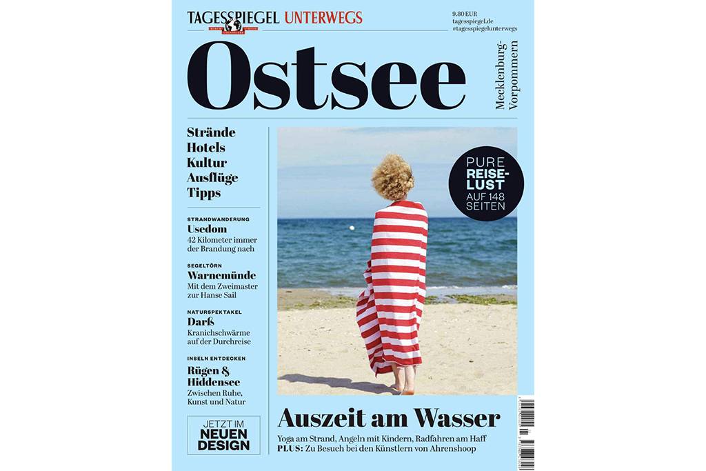 Back view of young woman wrapped in beach towel standing in front of the sea - TSFF00164