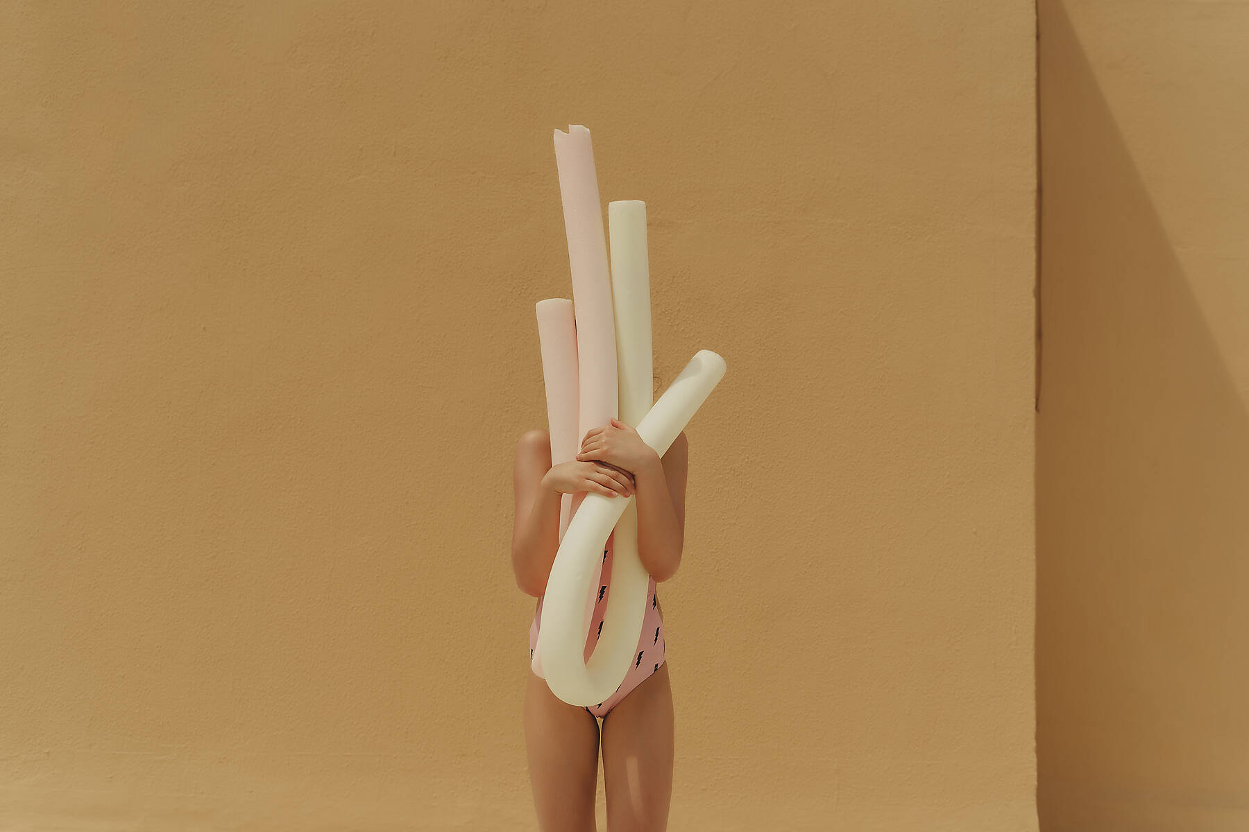 Girl in swimsuit hiding behind pool noodles, Royalty free image