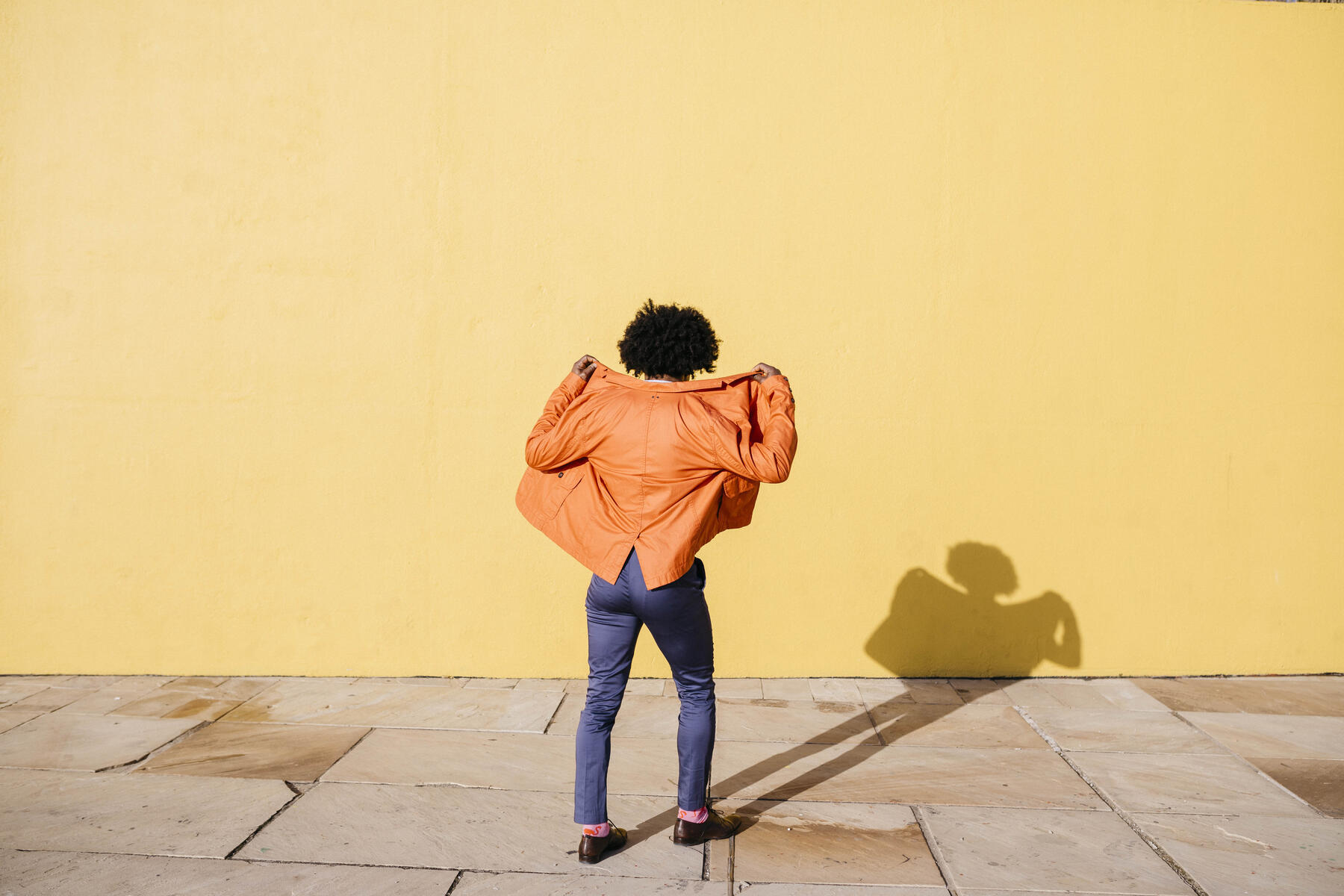 Back view of man wearing orange suit coat in front of yellow wall, royalty-free, stock image