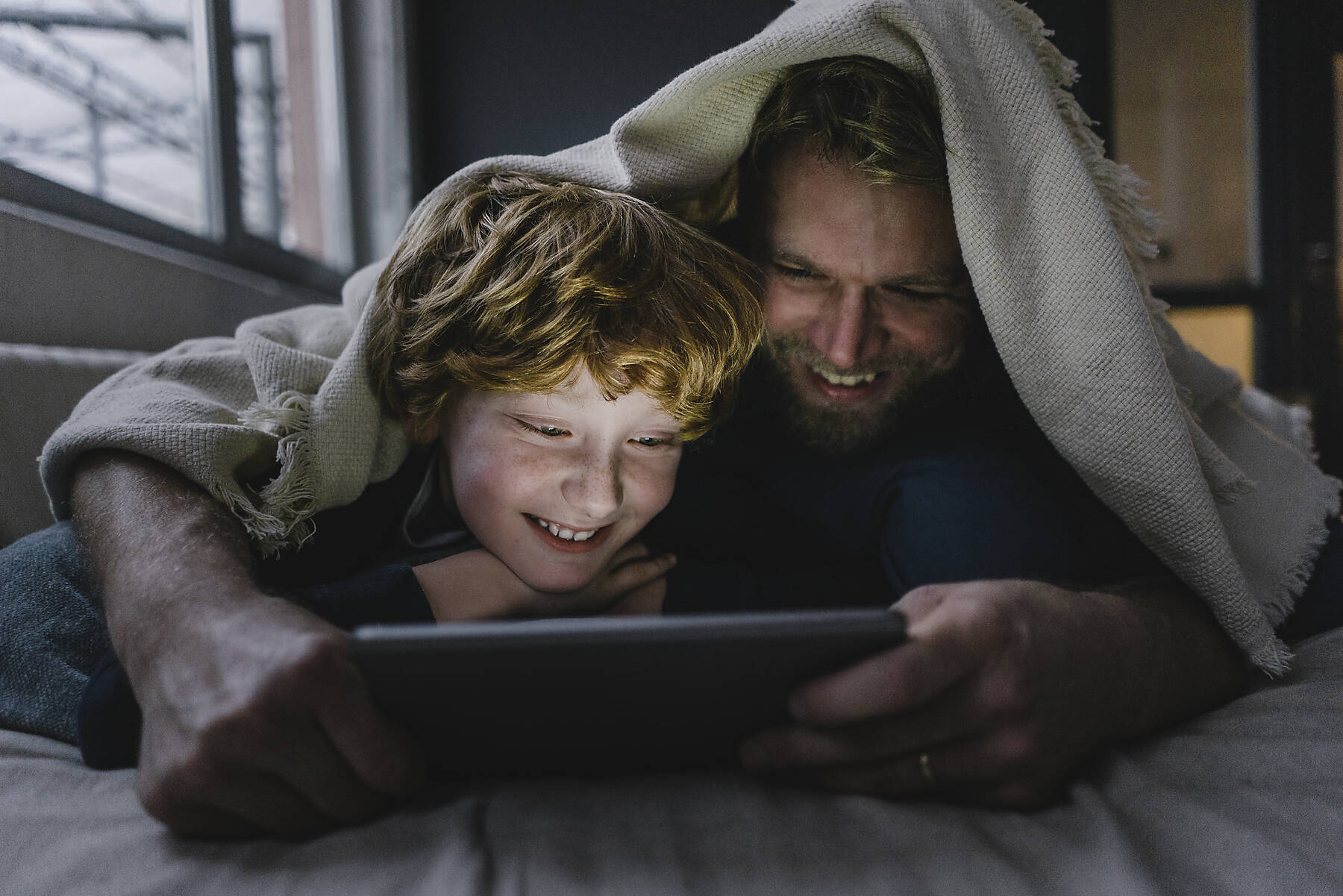 stockfoto, lizenzfrei, Vater und Sohn liegen zusammen unter einer Decke und schauen auf ein digitales Tablet