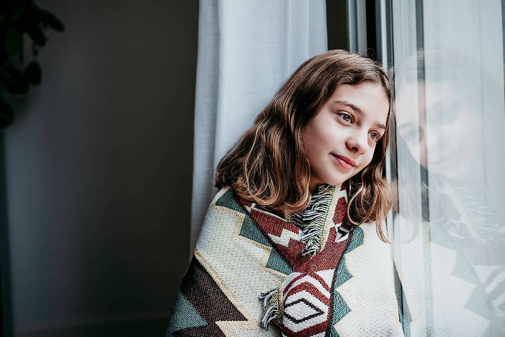 Girl covered in blanket smiling while sitting by window at home
Royalty free image