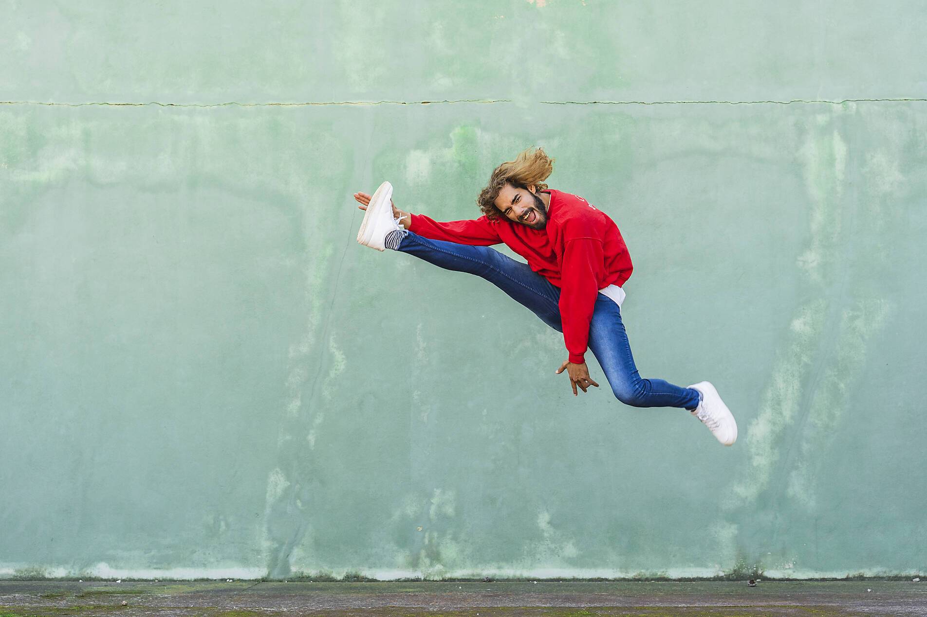 stock image, royalty-free, Portrait of young man in wearing red sweatshirt jumping in the air in front of green wall