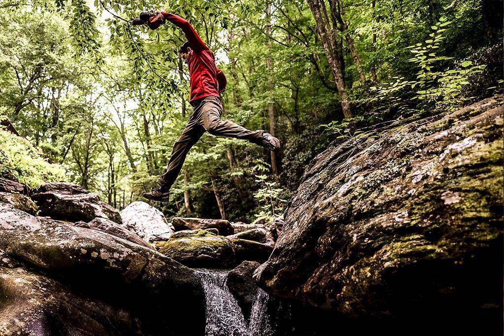 stock image, royalty-free, Low angle view of hiker leaping over rocks in forest