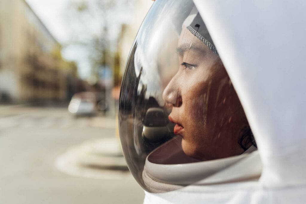 Junge weibliche Astronautin mit Weltraumhelm, die an einem sonnigen Tag wegschaut