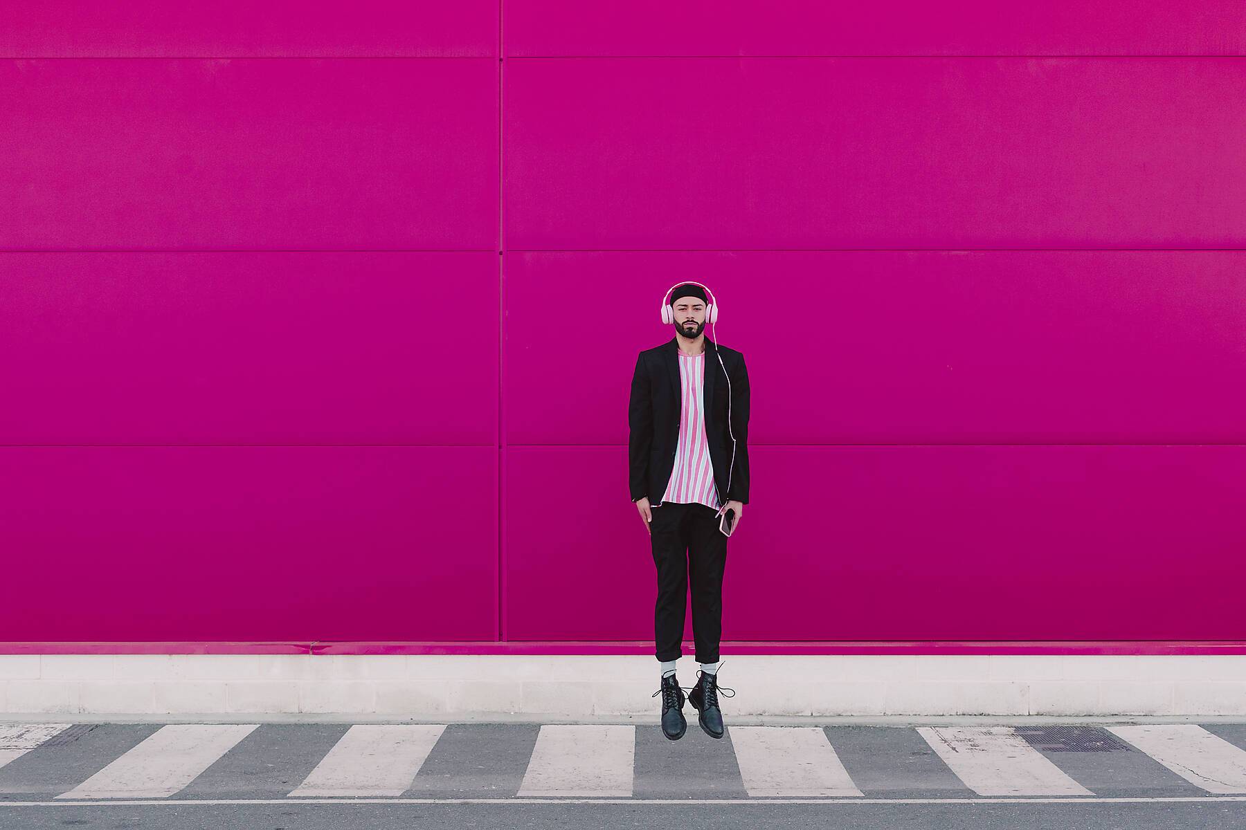 stock image, royalty-free, young man with headphones jumping in front of a pink wall