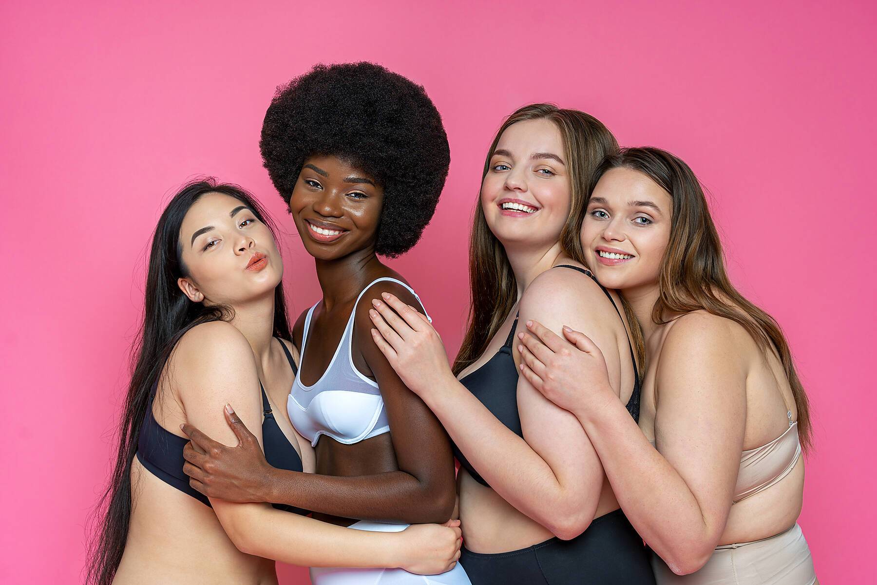 stock image, royalty-free, Smiling group of multi-ethnic female models in lingerie embracing each other against pink background