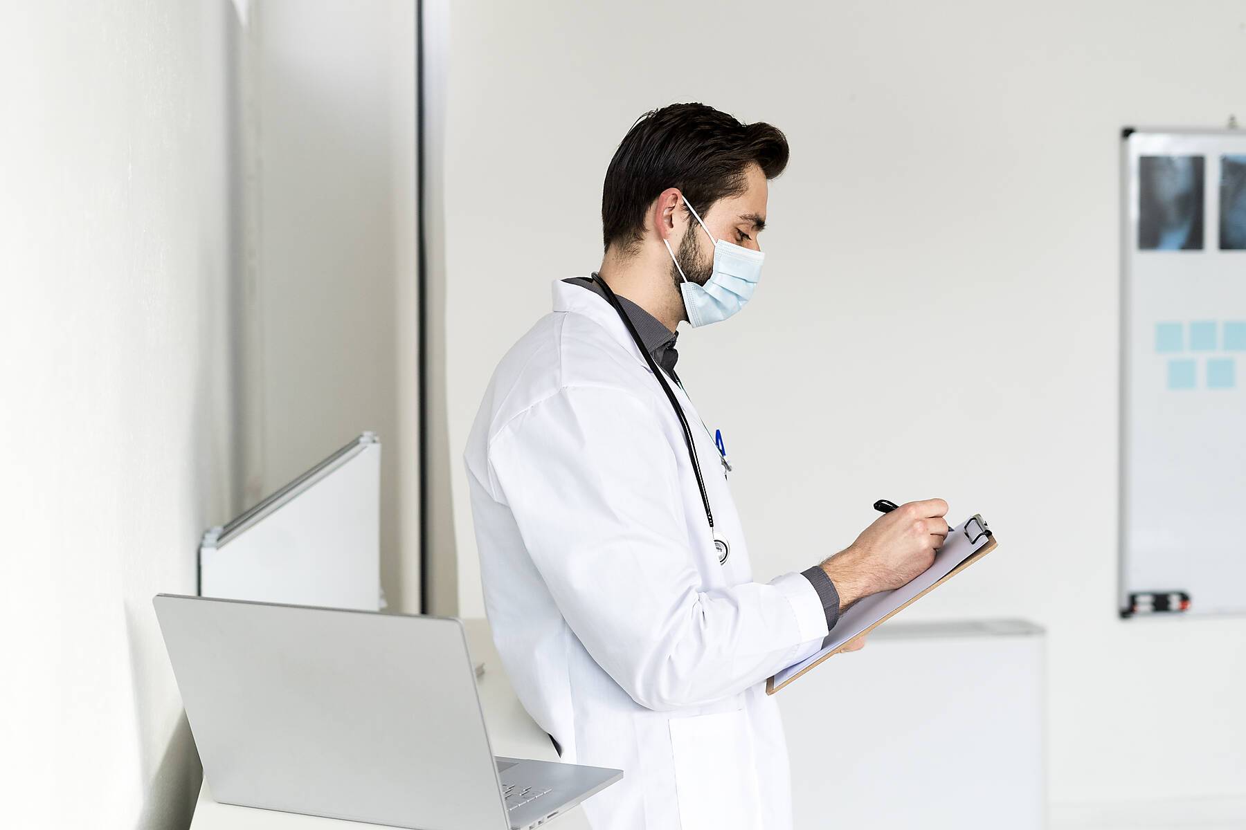 Male doctor writing on clipboard in hospital during COVID-19
