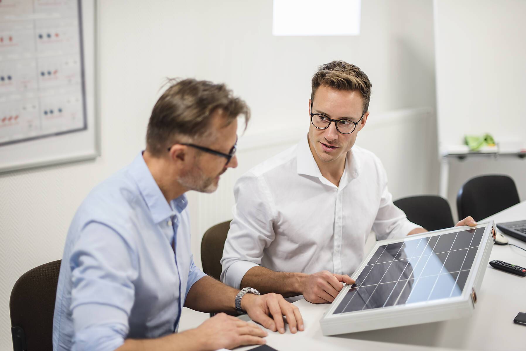Stockfoto, lizenzfrei, Zwei Geschäftsleute untersuchen Solarpanel auf Schreibtisch im Büro