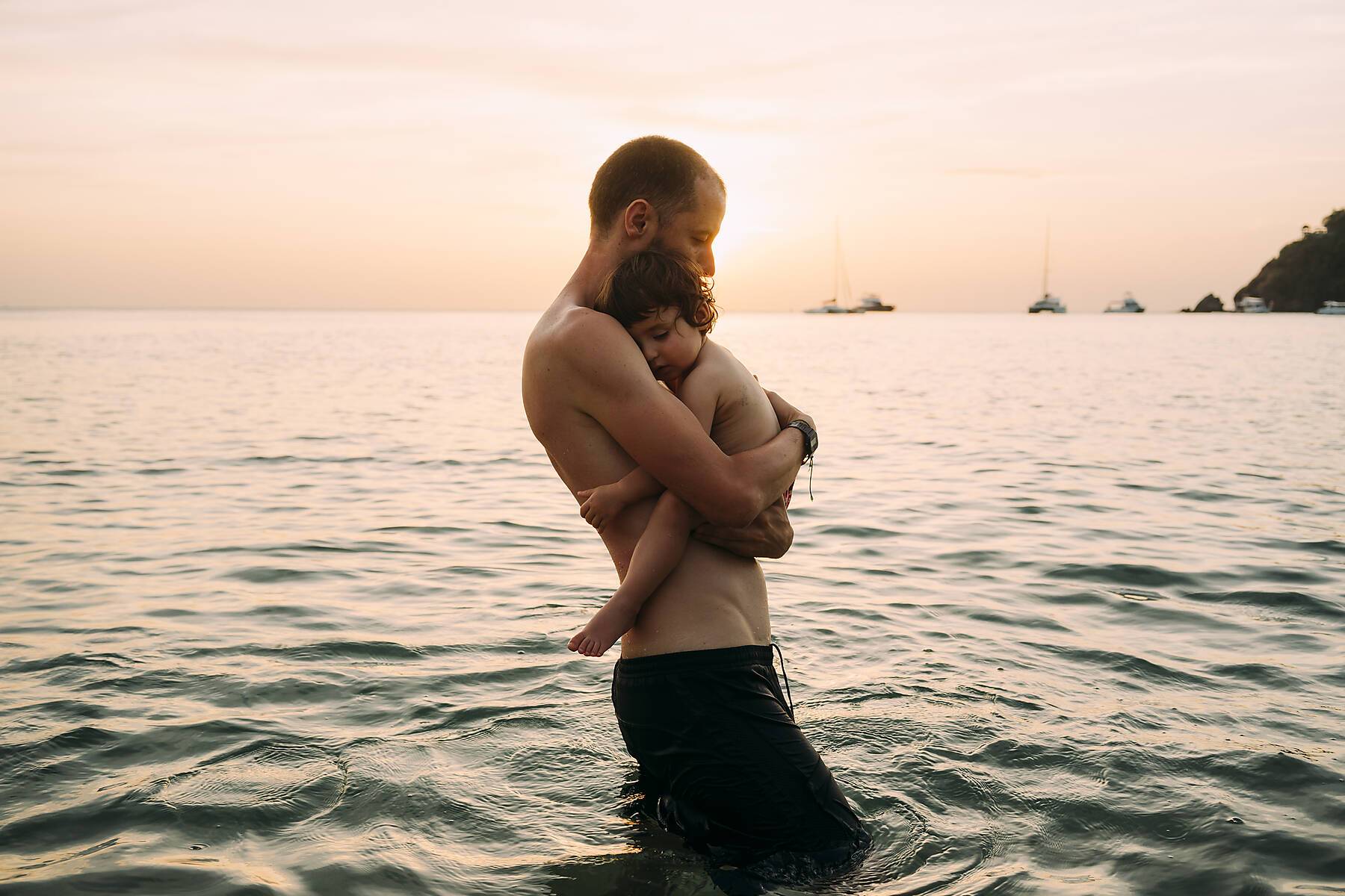 Man carrying little daughter on his arms while wading in the sea