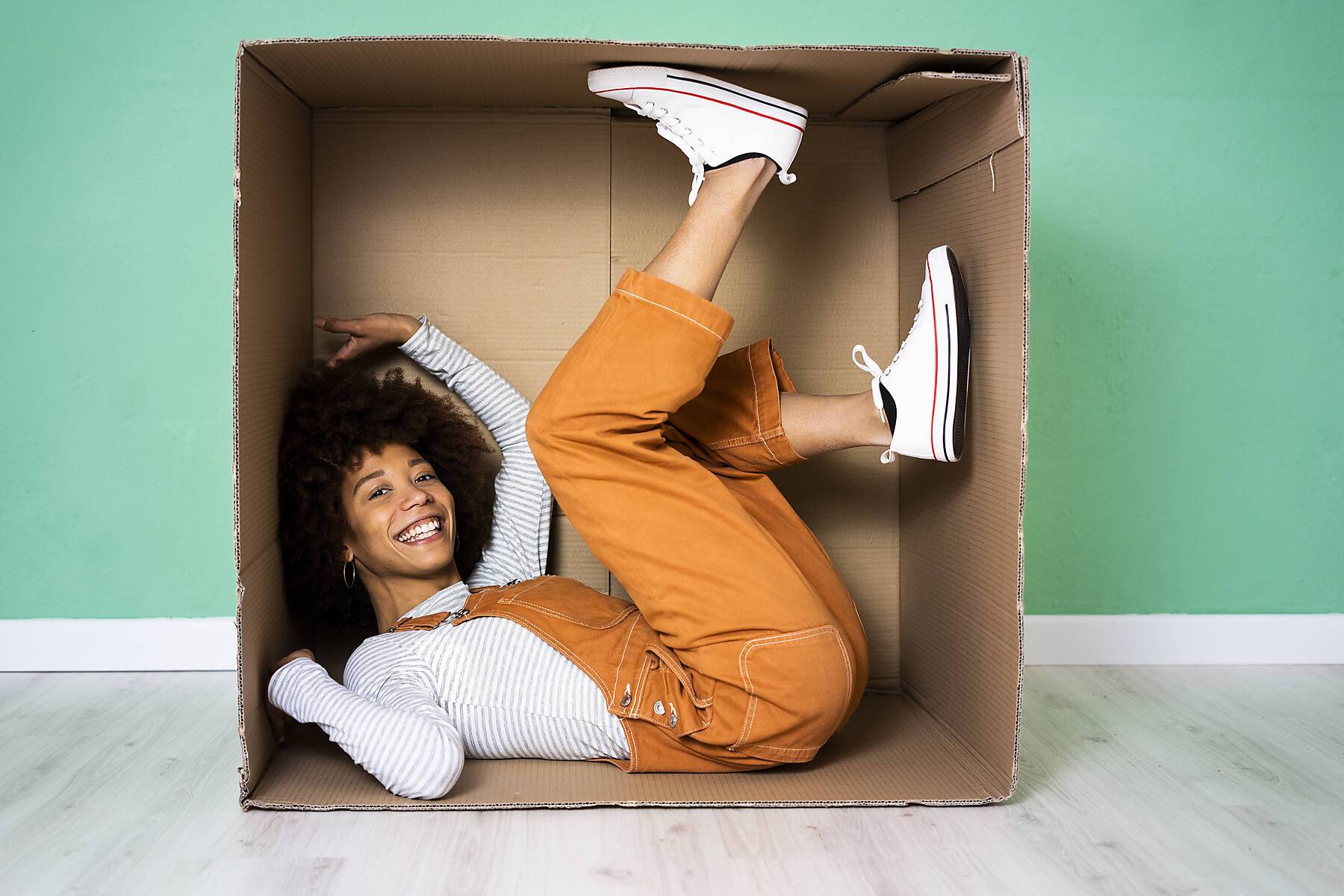 stock image, royalty-free, Cheerful woman lying in cardboard box against green wall in new loft apartment