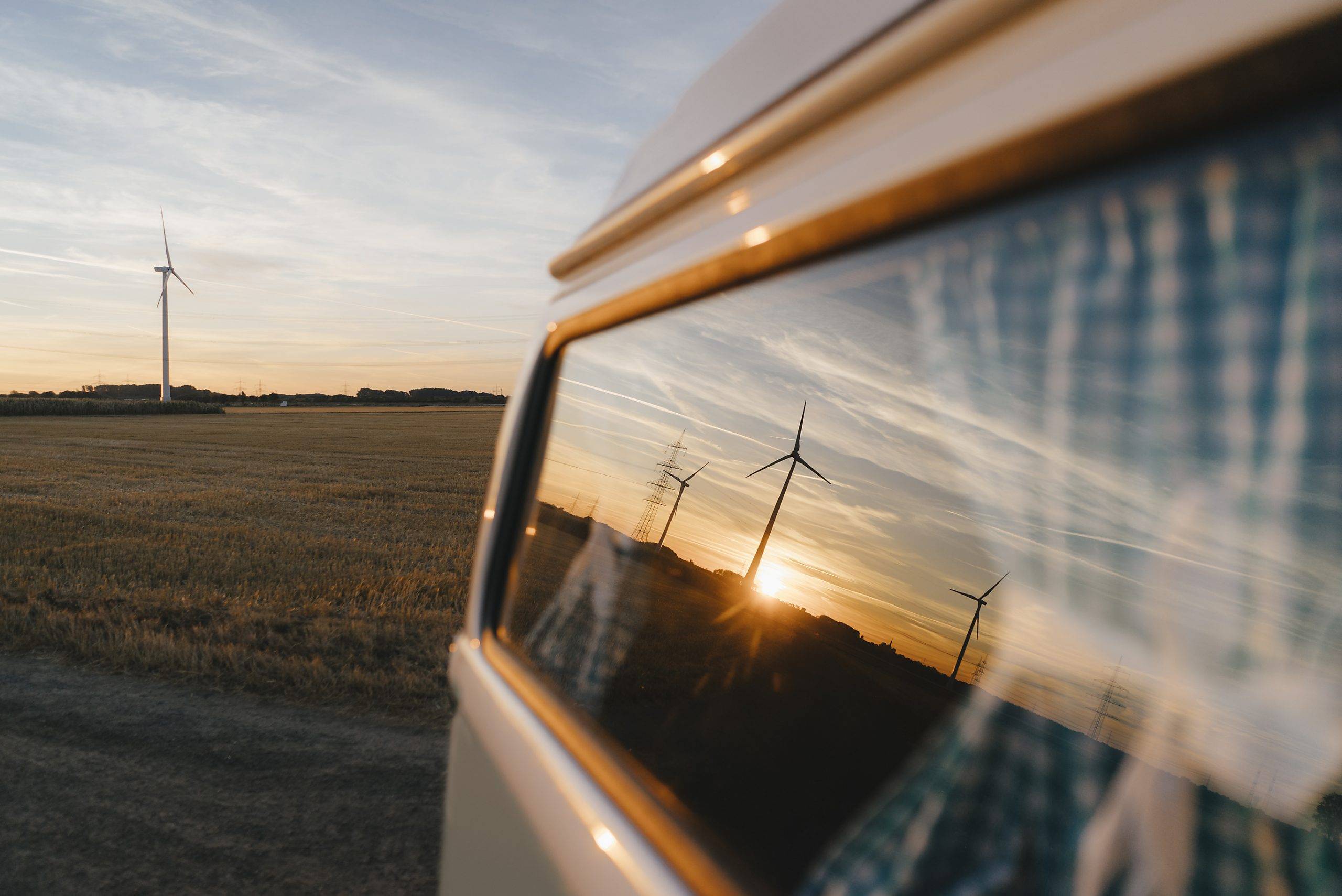 Stockfoto, lizenzfrei, Wohnmobil in ländlicher Landschaft mit Windrädern bei Sonnenuntergang