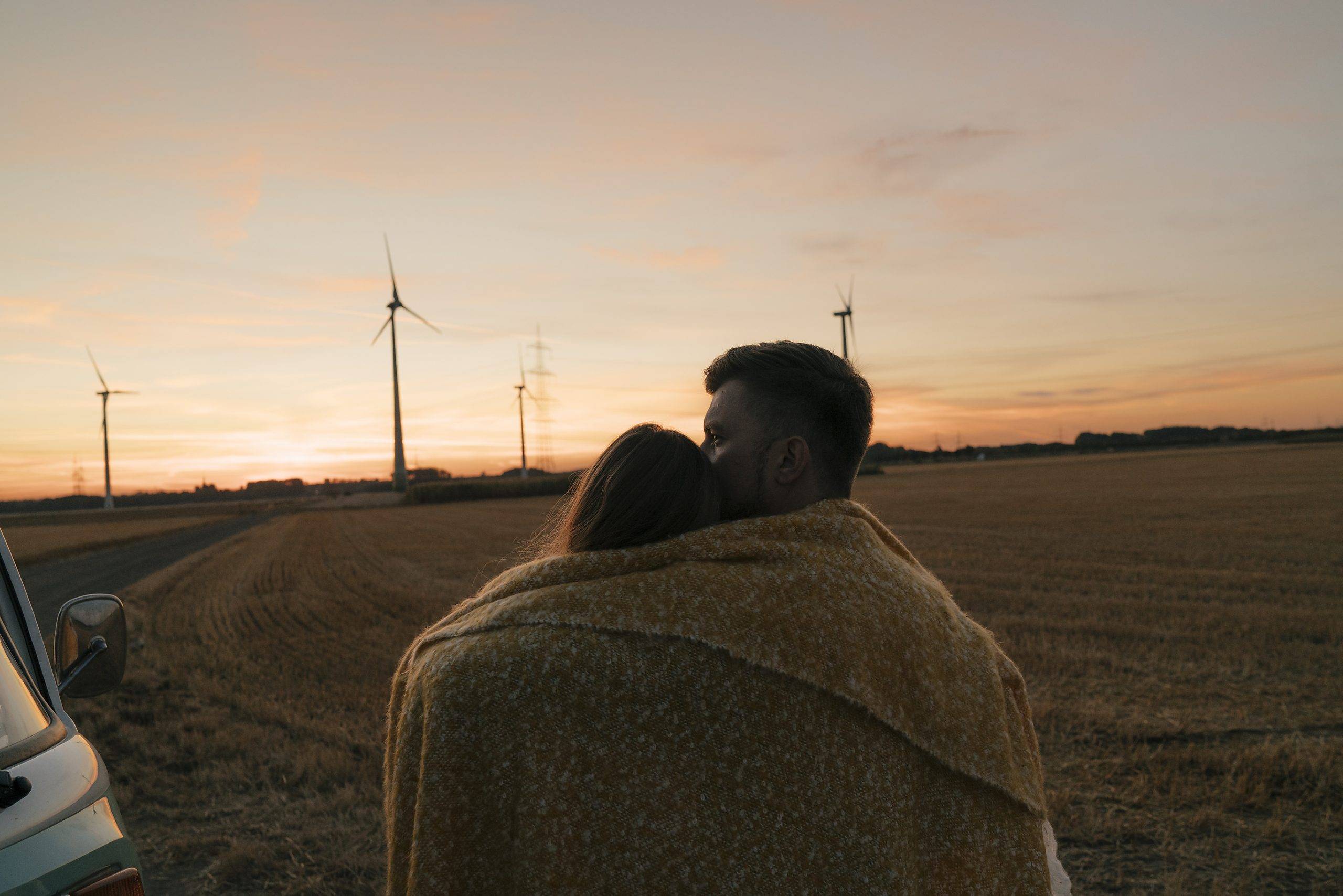 Stockfoto, lizenzfrei, Stockfoto, lizenzfrei, Paar in einer Decke eingewickelt am Wohnmobil in ländlicher Landschaft mit Windrädern im Hintergrund