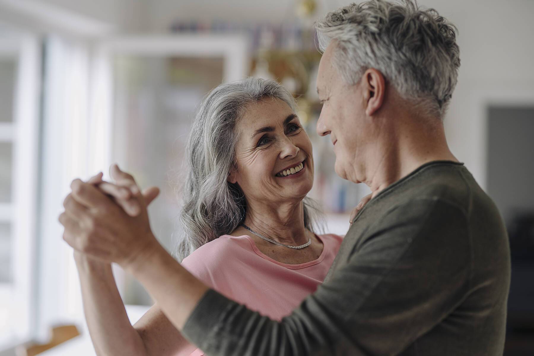 Happy senior couple dancing in living room at home