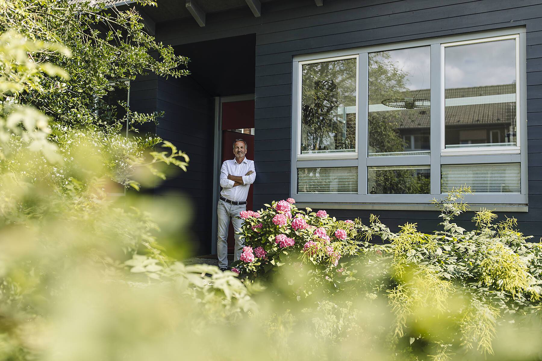 Stock Image, royalty-free, Man with arms crossed leaning on wall outside house during sunny day