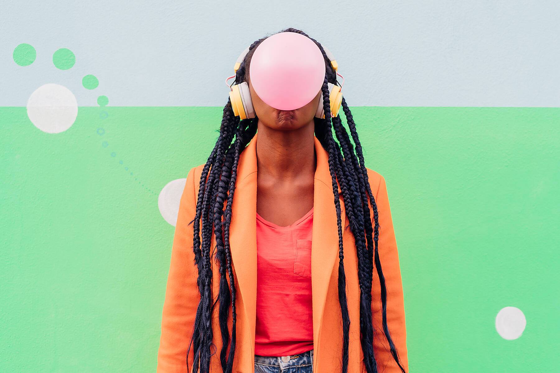 Italy, Milan, Stylish woman with headphones blowing gum against wall