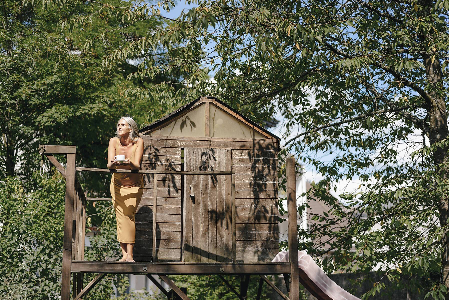 Woman with cup of coffee in front of tree house enjoying sunlight