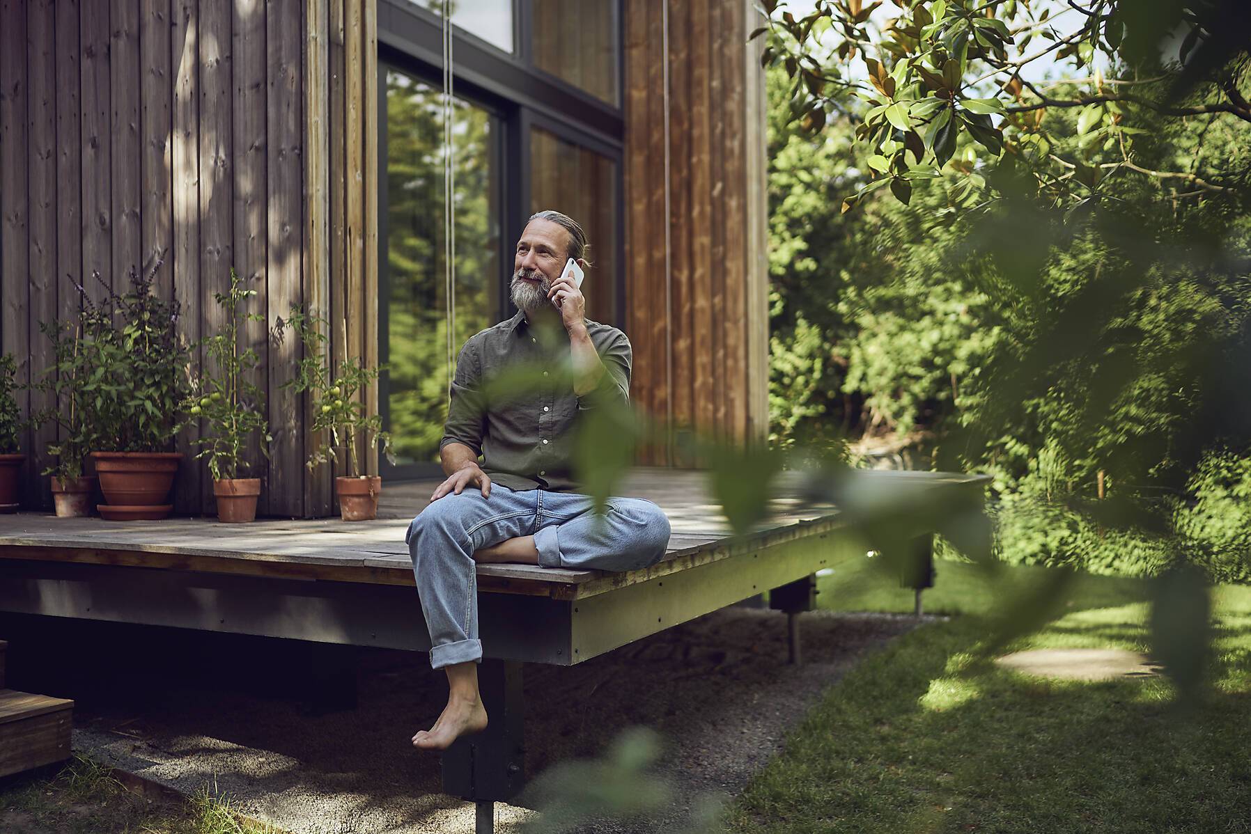 Stock Image, royalty-free. Mature man looking away while talking over mobile phone outside tiny house