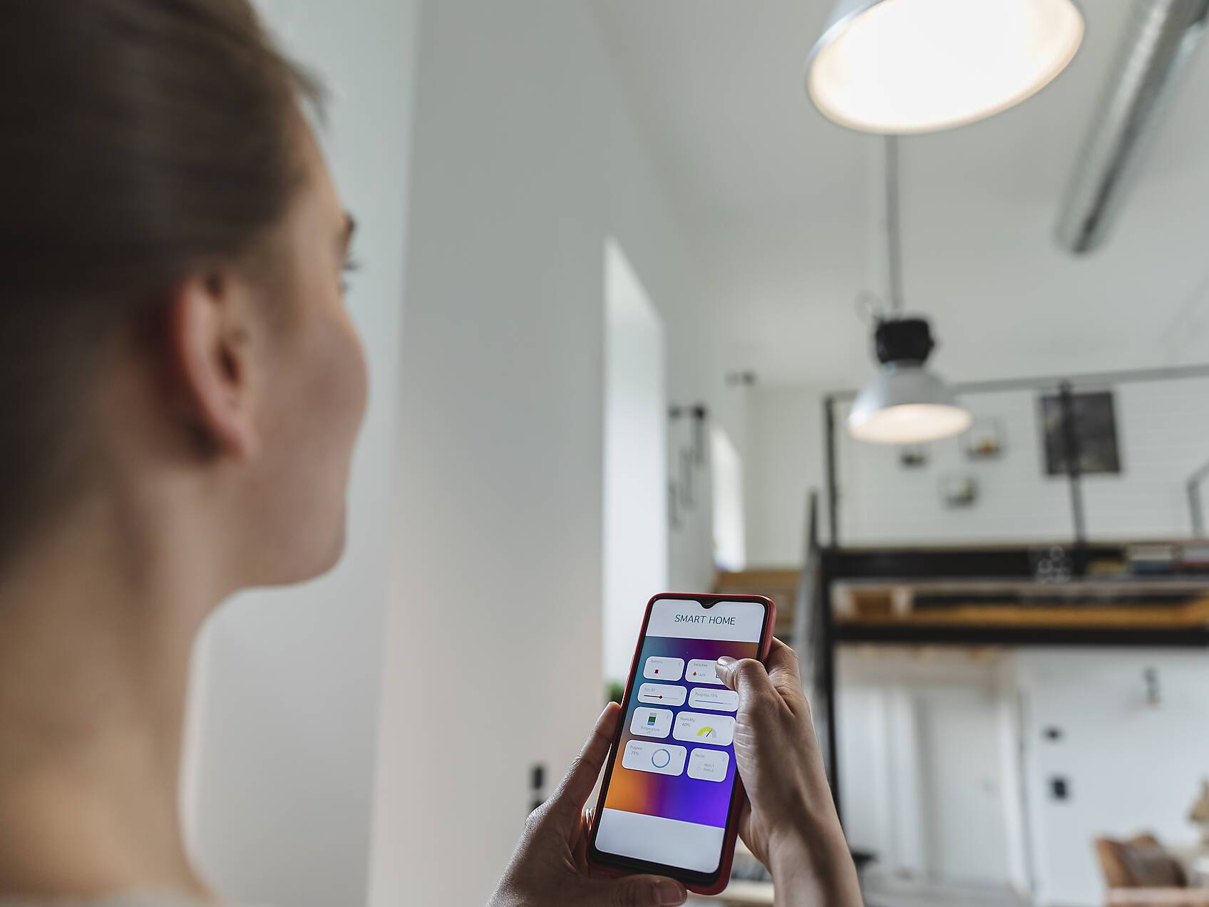 Stockfoto, lizenzfrei, Junge Frau, die das Licht mit einem Mobiltelefon zu Hause steuert